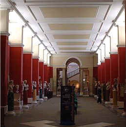 an impressive sculpture gallery with many Roman classical sculptures on view set against crimson red walls