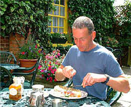 The courtyard has green metal tables and green chairs and has a variety of very cheerful potted tubs of brightly coloured summer flowers.